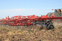 A red tractor with a plow in the middle of it.