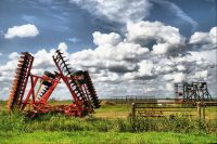 A red tractor sitting in the grass under a cloudy sky.