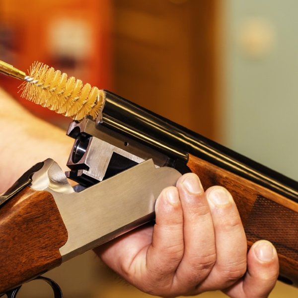 A person holding a rifle with a cleaning brush.