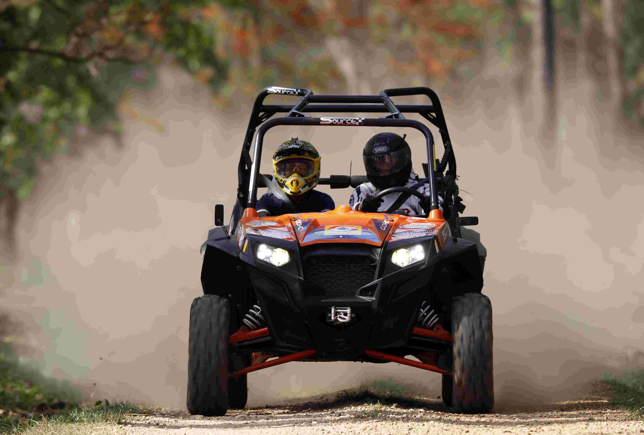 Two people in a buggy driving on the dirt.