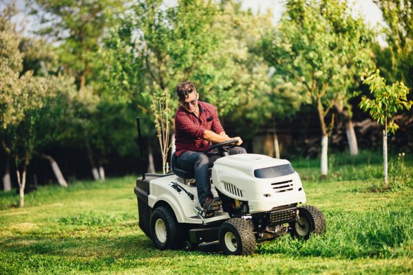 A man riding on the back of a white lawn mower.