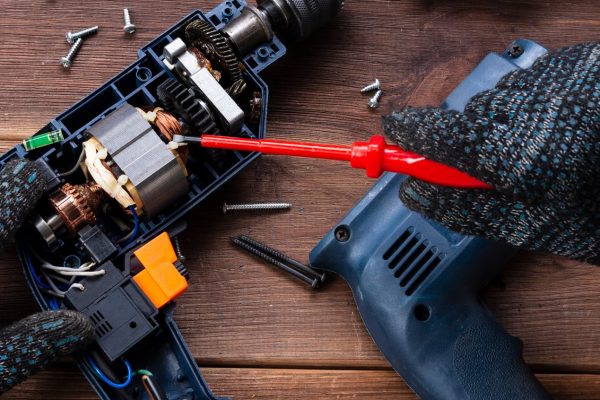 A person using a pair of red pliers to fix an electric drill.