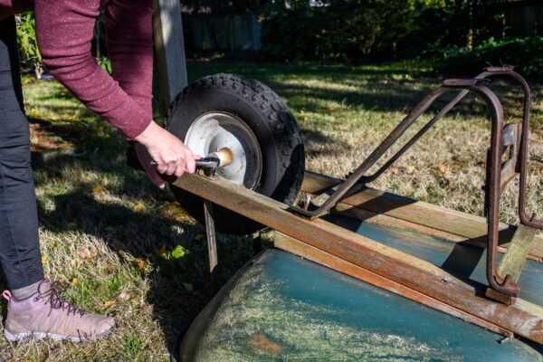 A person is using an old tire to lift the back of a wooden cart.