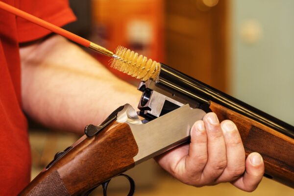 A person holding a rifle and cleaning it with a brush.