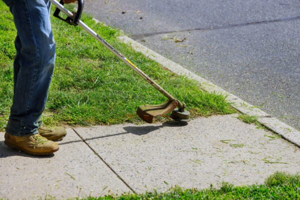 A person with a weed trimmer on the sidewalk.