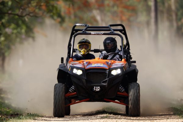 Two people in a buggy driving on dirt road.