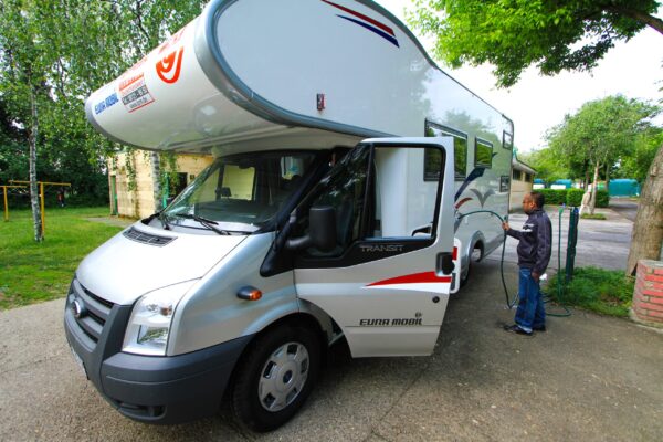 A man standing next to an rv parked on the side of road.