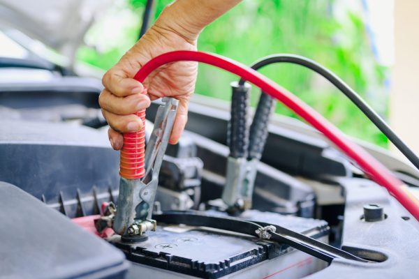 A person holding a red hose and a car battery.